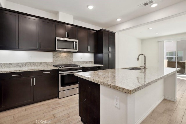 kitchen featuring light stone counters, stainless steel appliances, visible vents, a sink, and light wood-type flooring