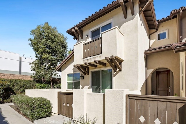 exterior space featuring a fenced front yard, a tiled roof, a balcony, and stucco siding