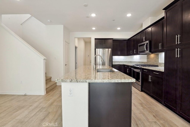 kitchen featuring appliances with stainless steel finishes, a sink, light wood-style flooring, and light stone countertops