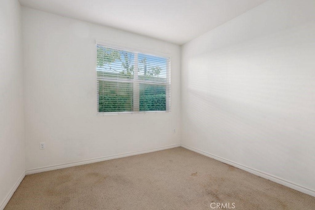 spare room with baseboards and light colored carpet