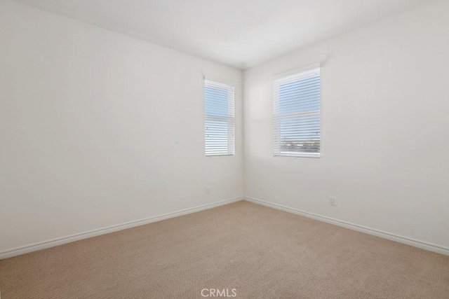 unfurnished room featuring light carpet and baseboards