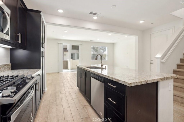 kitchen featuring light wood finished floors, a center island with sink, visible vents, stainless steel appliances, and a sink