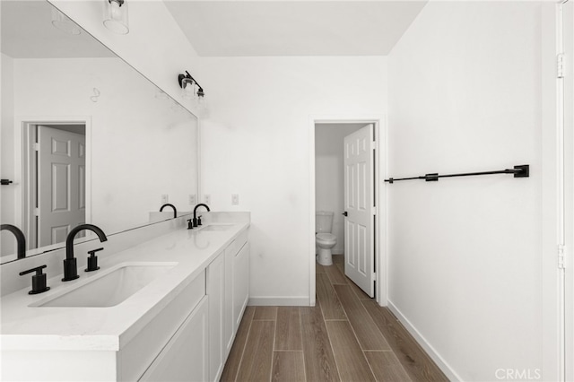 full bath with a sink, toilet, double vanity, and wood tiled floor