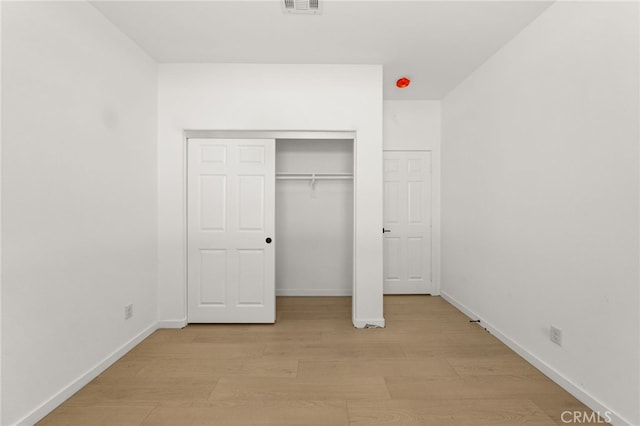 unfurnished bedroom featuring light wood-style flooring, baseboards, visible vents, and a closet