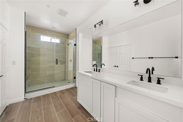 bathroom with a sink, a shower stall, wood tiled floor, and double vanity