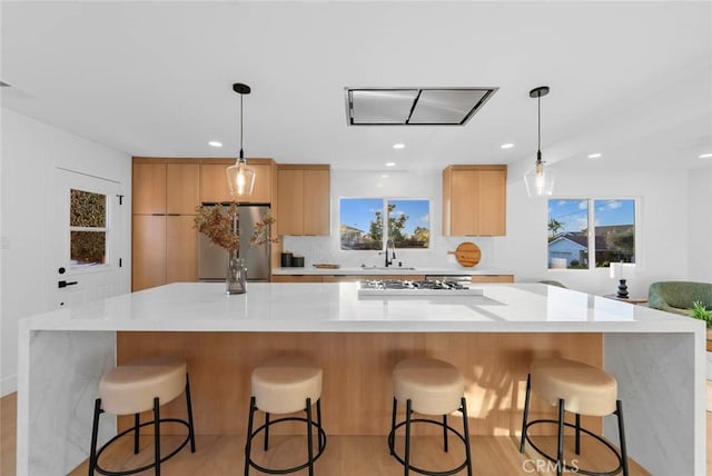 kitchen with stainless steel fridge, a large island, a sink, gas stovetop, and backsplash