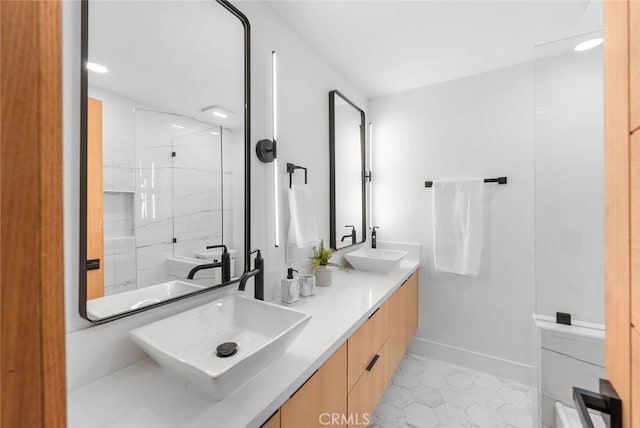 full bathroom with double vanity, a marble finish shower, baseboards, tile patterned floors, and a sink