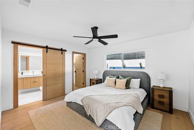 bedroom featuring light wood-style floors, a ceiling fan, baseboards, and a barn door