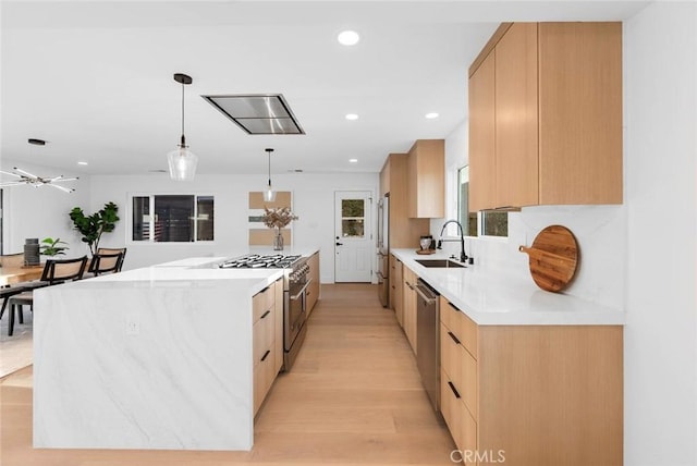 kitchen featuring light brown cabinetry, appliances with stainless steel finishes, a kitchen island, a sink, and modern cabinets