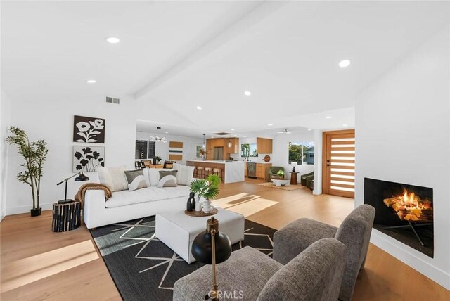 living area featuring vaulted ceiling with beams, a warm lit fireplace, light wood-style flooring, recessed lighting, and visible vents