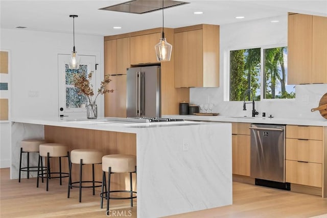 kitchen with modern cabinets, a breakfast bar area, stainless steel appliances, light wood-type flooring, and a sink