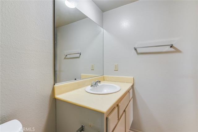 half bath with toilet, a textured wall, and vanity