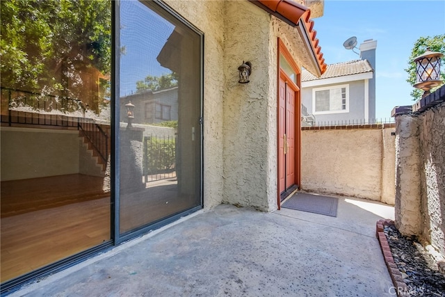 entrance to property featuring a tiled roof, fence, a patio, and stucco siding