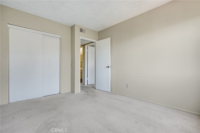 unfurnished bedroom featuring light carpet, a textured ceiling, a closet, and visible vents