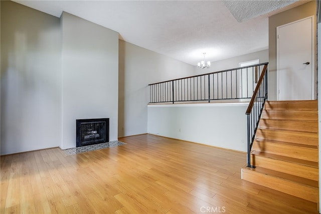 unfurnished living room featuring a fireplace with flush hearth, wood finished floors, stairs, a textured ceiling, and a chandelier