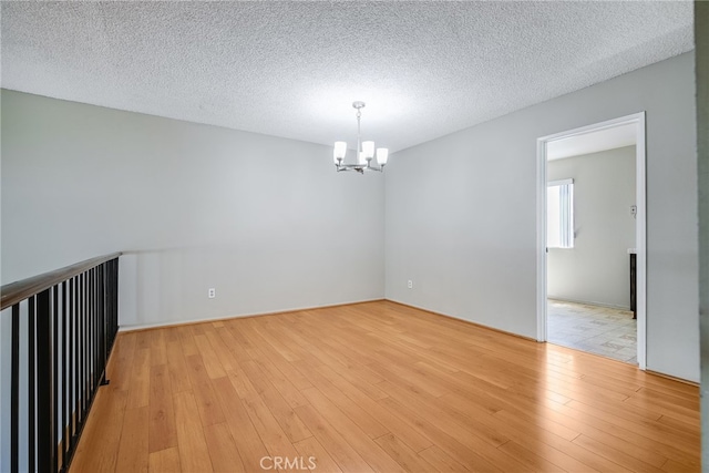 spare room with light wood-style floors, a textured ceiling, and an inviting chandelier