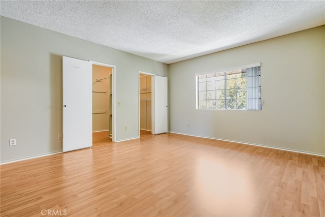 unfurnished bedroom featuring baseboards, a walk in closet, a textured ceiling, light wood-type flooring, and a closet