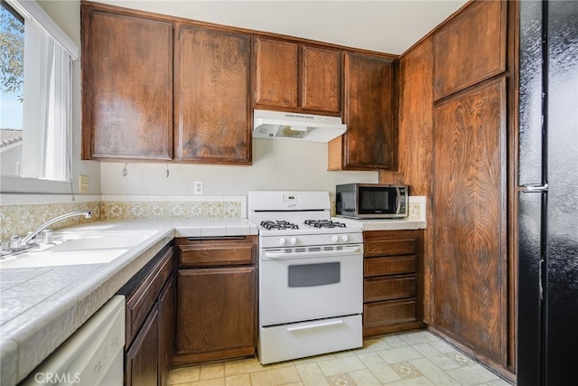 kitchen with tile countertops, under cabinet range hood, white appliances, and a sink