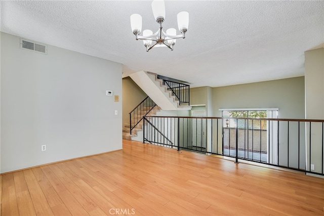 spare room featuring visible vents, wood finished floors, stairs, a textured ceiling, and a chandelier