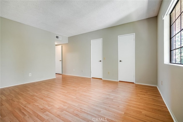 empty room featuring light wood-type flooring, baseboards, visible vents, and a textured ceiling