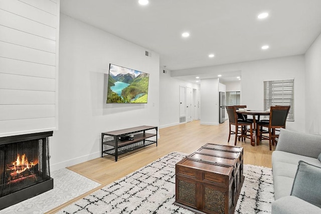 living area featuring a warm lit fireplace, recessed lighting, visible vents, and light wood-style floors