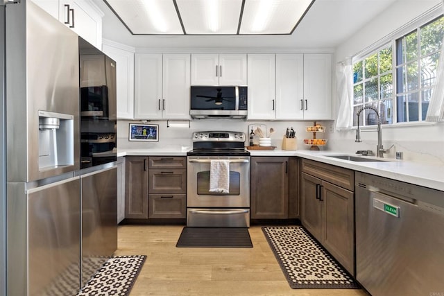 kitchen featuring light countertops, appliances with stainless steel finishes, white cabinetry, a sink, and light wood-type flooring