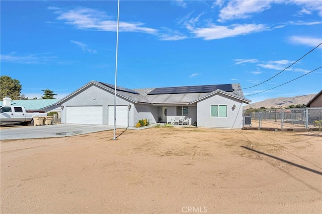 ranch-style home featuring stucco siding, roof mounted solar panels, fence, a garage, and driveway