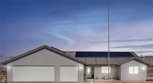 single story home featuring a garage, driveway, roof mounted solar panels, and stucco siding