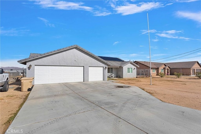 ranch-style house featuring solar panels, concrete driveway, an attached garage, fence, and stucco siding