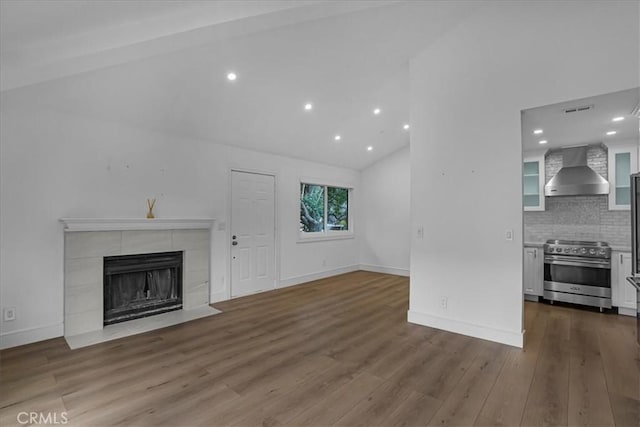 unfurnished living room featuring lofted ceiling, a fireplace, baseboards, and wood finished floors