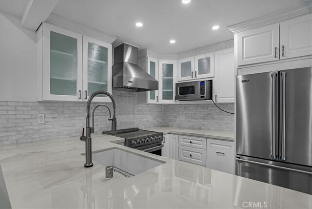 kitchen with appliances with stainless steel finishes, white cabinets, a sink, and wall chimney exhaust hood