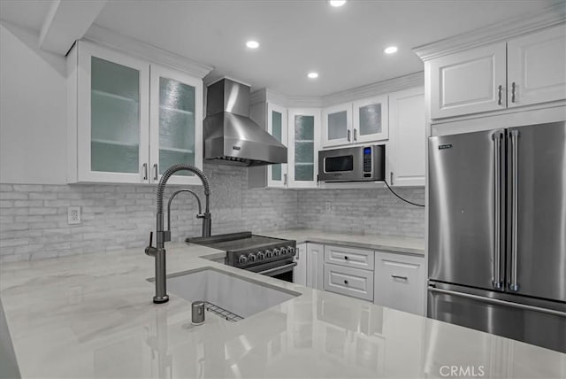 kitchen featuring stainless steel appliances, white cabinets, wall chimney exhaust hood, and a sink