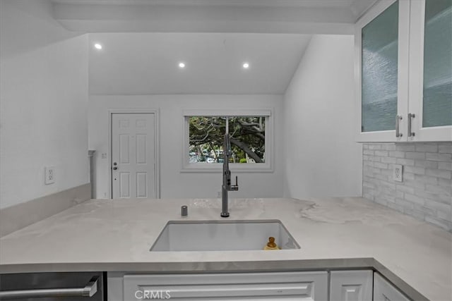 kitchen with lofted ceiling, a sink, white cabinetry, backsplash, and glass insert cabinets