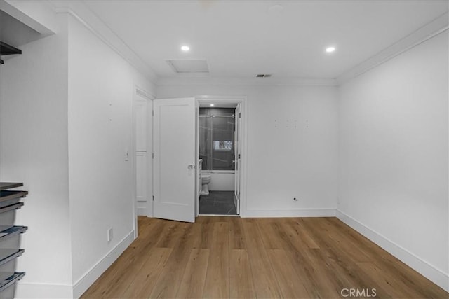 empty room with wood finished floors, visible vents, baseboards, ornamental molding, and attic access