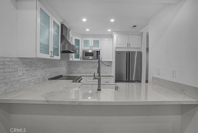 kitchen featuring decorative backsplash, wall chimney exhaust hood, a peninsula, stainless steel appliances, and a sink