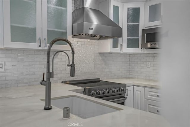 kitchen with white cabinets, decorative backsplash, light countertops, wall chimney range hood, and a sink