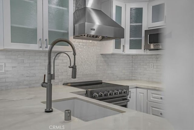 kitchen featuring wall chimney range hood, white cabinetry, light countertops, a sink, and decorative backsplash