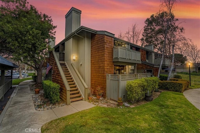 property exterior at dusk with fence, a lawn, a chimney, and stairs