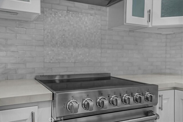 details featuring light countertops, decorative backsplash, stainless steel range with electric stovetop, and white cabinets