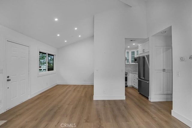 unfurnished living room featuring light wood finished floors, baseboards, high vaulted ceiling, and recessed lighting