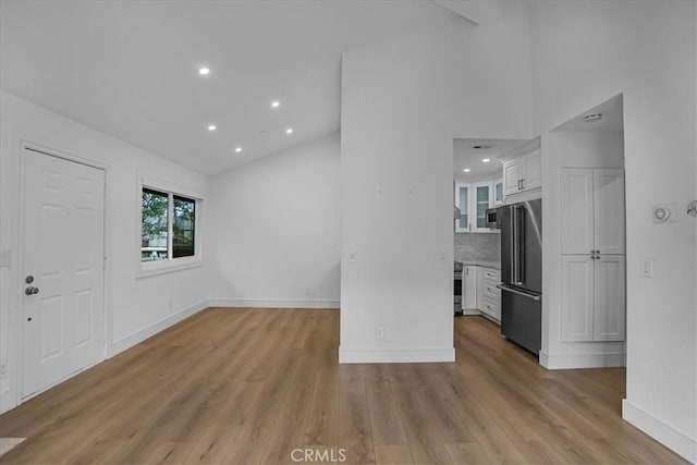 interior space with light wood-type flooring, high vaulted ceiling, baseboards, and recessed lighting