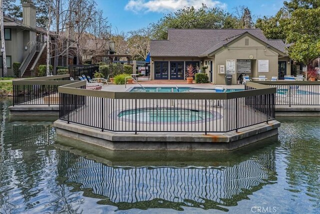 rear view of property with a patio area, a water view, a community pool, and stucco siding