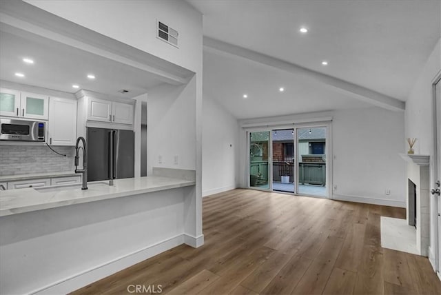 unfurnished living room with a sink, wood finished floors, a fireplace with flush hearth, visible vents, and baseboards