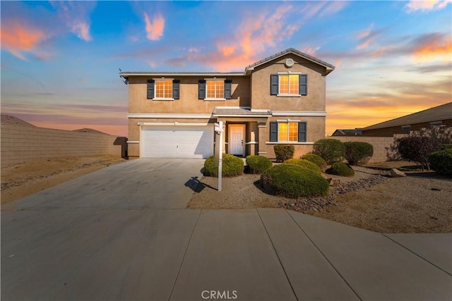 traditional-style home with a garage, driveway, fence, and stucco siding