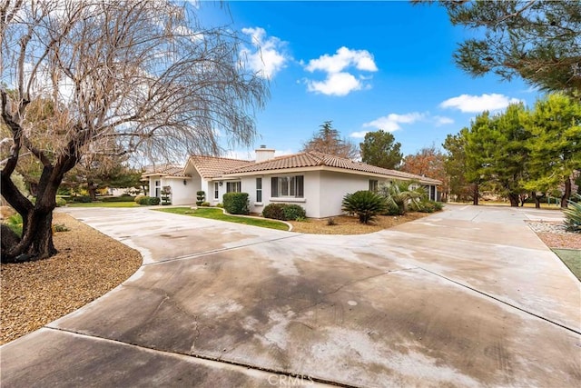 view of side of home with a tile roof, driveway, a chimney, and stucco siding