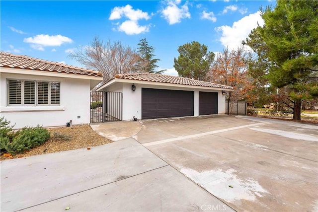 view of front of house featuring a gate, a detached garage, a tiled roof, and stucco siding