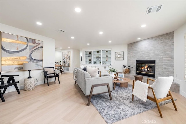 living area featuring light wood-style flooring, visible vents, a tiled fireplace, and recessed lighting