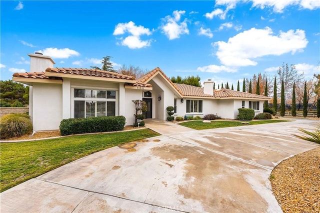 mediterranean / spanish-style home with concrete driveway, a chimney, a front lawn, and stucco siding