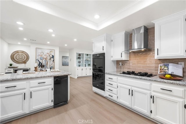 kitchen featuring black appliances, wall chimney range hood, backsplash, and white cabinetry