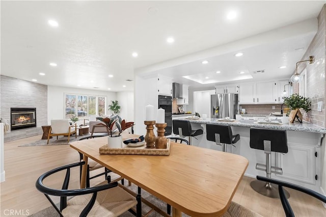 dining space with light wood finished floors, visible vents, a large fireplace, and recessed lighting